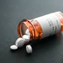 An open bottle of pills lying sideways with some pills coming out of it