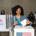 A young woman casting her vote by placing a ballot in a polling box during the U.S. elections.