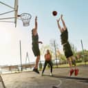 Cheerful athletic people spending time together outdoors on playground, playing basketball on a sunny day. Sport without gym during quarantine concept. Horizontal shot
