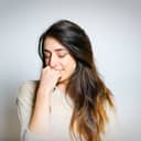 portrait of a shy brunette girl that's slightly smiling and looking down, with her hand close to her face