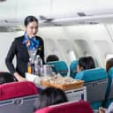 smiling flight attendant serving food and drinks to airplane passengers, pushing a service cart down the aisle