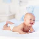 happy newborn baby in a diaper enjoying tummy time on the bed with a blue toy bear in background