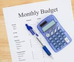 Pen and calculator on a piece of paper reading "Monthly Budget"
