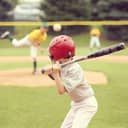 kid in safety gear swinging a bat on a baseball field with other players in the background