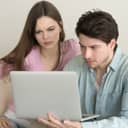 young couple appearing worried as they use a laptop to check something online