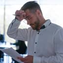 An upset man reading a text from a piece of paper while holding a pen