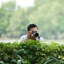 A man taking a photo with his camera behind a hedge