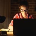 a young woman working on her laptop late at night in her room