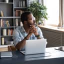 businessman sitting in his home office with a laptop in front of him, gazing into the distance
