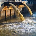 An industrial discharge pipe releasing factory wastewater directly into a river.
