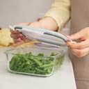 close-up of a woman securing the lid on a glass container at a white marble kitchen table