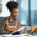 young female business owner writing something in her notebook with laptop in front of her