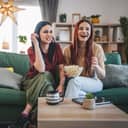 two happy sisters sitting on a sofa enjoying a movie or TV series at home and eating popcorn