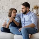 Serious father listen to his pre-teen little son talking seated on sofa at home, speaking spend time together at home. Cute boy share problems, ask advice to dad. Communication, care and trust concept