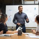 A composed male executive leading a corporate briefing, addressing his team in a boardroom during a meeting.
