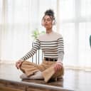 portrait of a young woman using headphones for guided meditation, seated on the floor of her living room with eyes closed