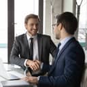 Two businessmen sitting at a table shaking hands