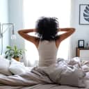 back view of a woman with curly hair stretching on the edge of her bed in the morning as she wakes up