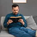 Close-up of a man reading a book while comfortably seated on a sofa at home.