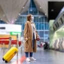 A female traveler holding a suitcase and wearing a mask looking at arrival-departure boards at a terminal