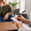 young man undergoing a psychology session with a female therapist at a clinic, close-up on her hands writing something down