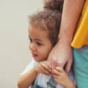 A closeup of a little girl hiding behind her mother
