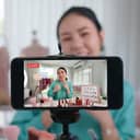 Woman recording herself on smartphone in front of a selection of beauty products