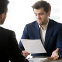 businessman dissatisfied with the paper he's reading, expressing disagreement while sitting across from his partner during the meeting