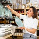 A young woman carefully selecting ceramic tableware in a store.
