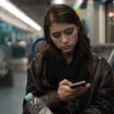 Girl with sad expression on her face using a smartphone while riding public transportation