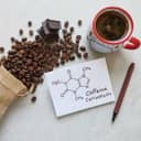 The structure of the caffeine molecule on a paper, with a rustic bag of spilled coffee beans scattered around and a cup of coffee.