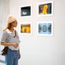 A young woman holds a digital tablet while examining framed artworks in an art gallery,