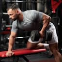 side view of a bodybuilder performing dumbbell rows on a bench, focusing on back muscles in a gym