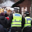 Back view of two police officers wearing high-visibility vests, managing the crowd at a public gathering in the UK.