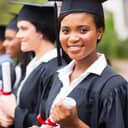 A female graduate holding her diploma looking at the camera with other graduates standing beside her in line