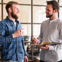 A smiling young male employee talking with another colleague, offering words of encouragement.