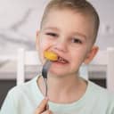 Close-up of a joyful child enjoying chicken nuggets at home.
