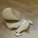 close-up of shattered pieces of a white ceramic vase on a wooden floor
