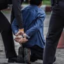 Man on his knees being handcuffed by a police officer with another officer standing close behind them