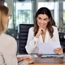 A cheerful middle-aged HR manager conducts a job interview with a female candidate, holding her CV.