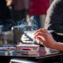 Close-up of a woman's hand holding a lit cigarette over an ashtray placed on a restaurant or cafe table.