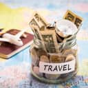 Closeup of a jar filled with change and banknotes with compass on top placed on a map. A model airplane on a passport can be seen in the background.