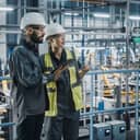 male specialist and female engineer wearing protective gear, talking and using a tablet at a car manufacturing facility