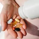 close-up of a woman's hand with supplements and a white bottle