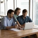 A business team of three discussing something, while looking at the laptop screen in the office.