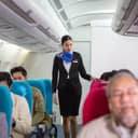 An Asian flight attendant walking down the plane aisle, ensuring passenger had fastened their seatbelts before take-off.