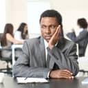 A businessman in a suit sitting alone away from his colleagues with a pensive expression on his face