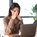 A woman sitting in front of a laptop with her hands over her face