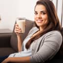 A girl sitting on a couch smiling with a glass of milk in her hand