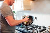 Man spraying cooking spray onto a pan in front of a stove in kitchen